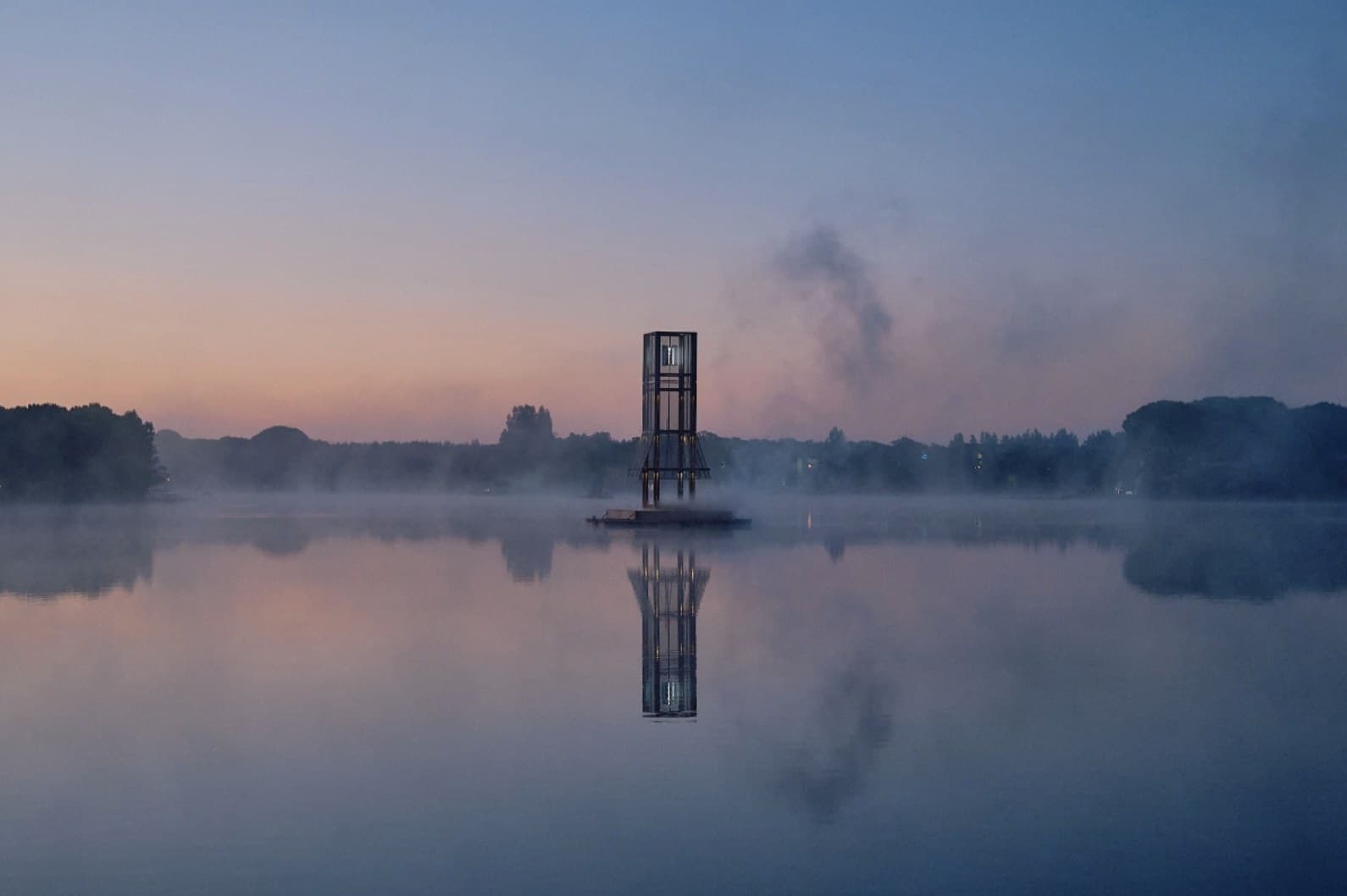 The same tower before sunrise, mist lying on a dead-calm lake and the whole structure repeated in the reflection